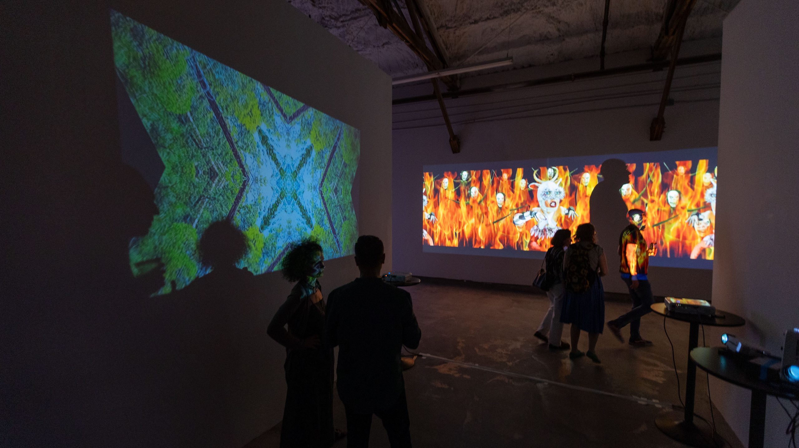 Two viewers in front of dual projections, kaleidoscope and figures in flame