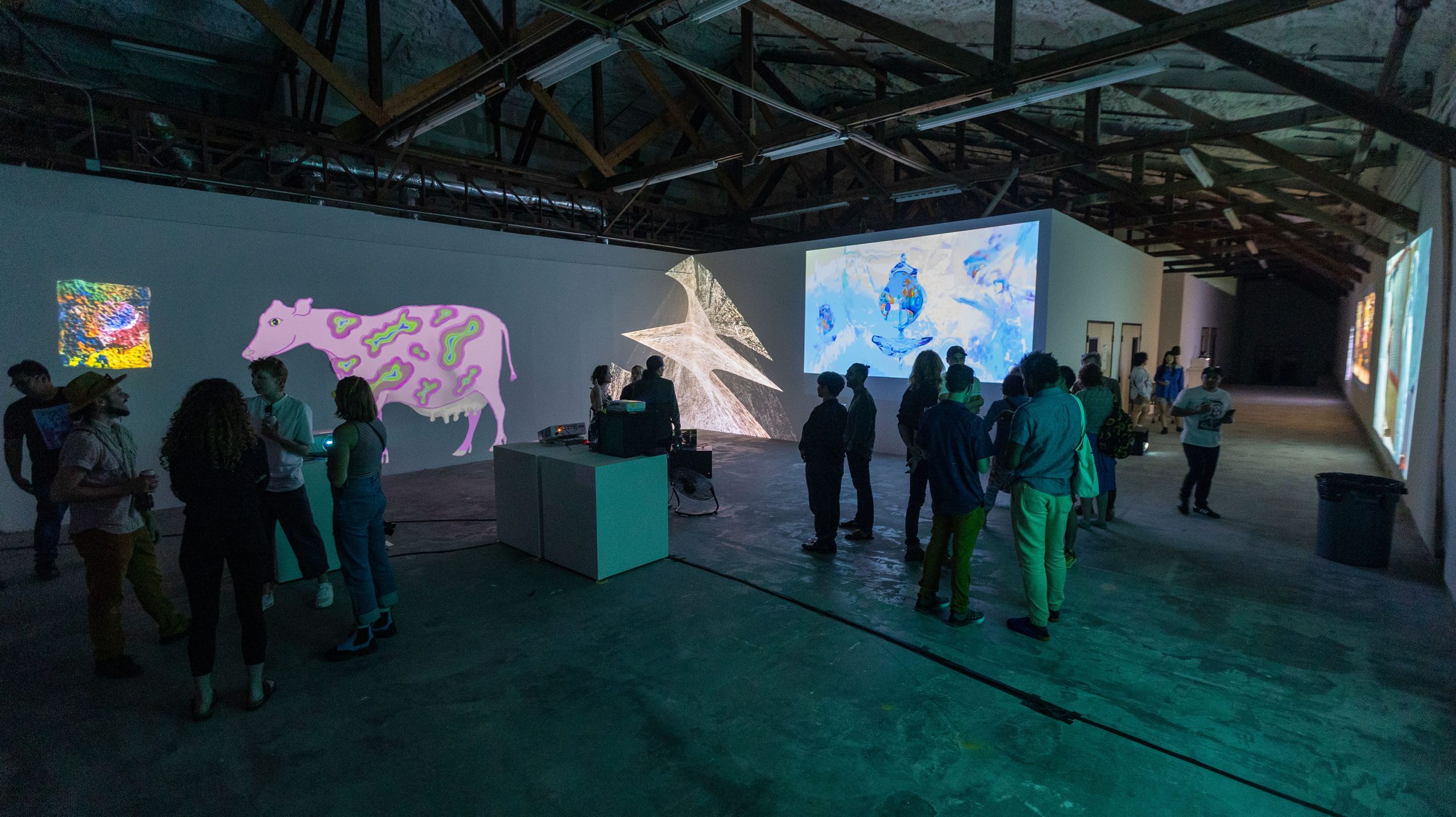 Crowd watching multi-screen install with painted cow, paper sculpture, and map projection
