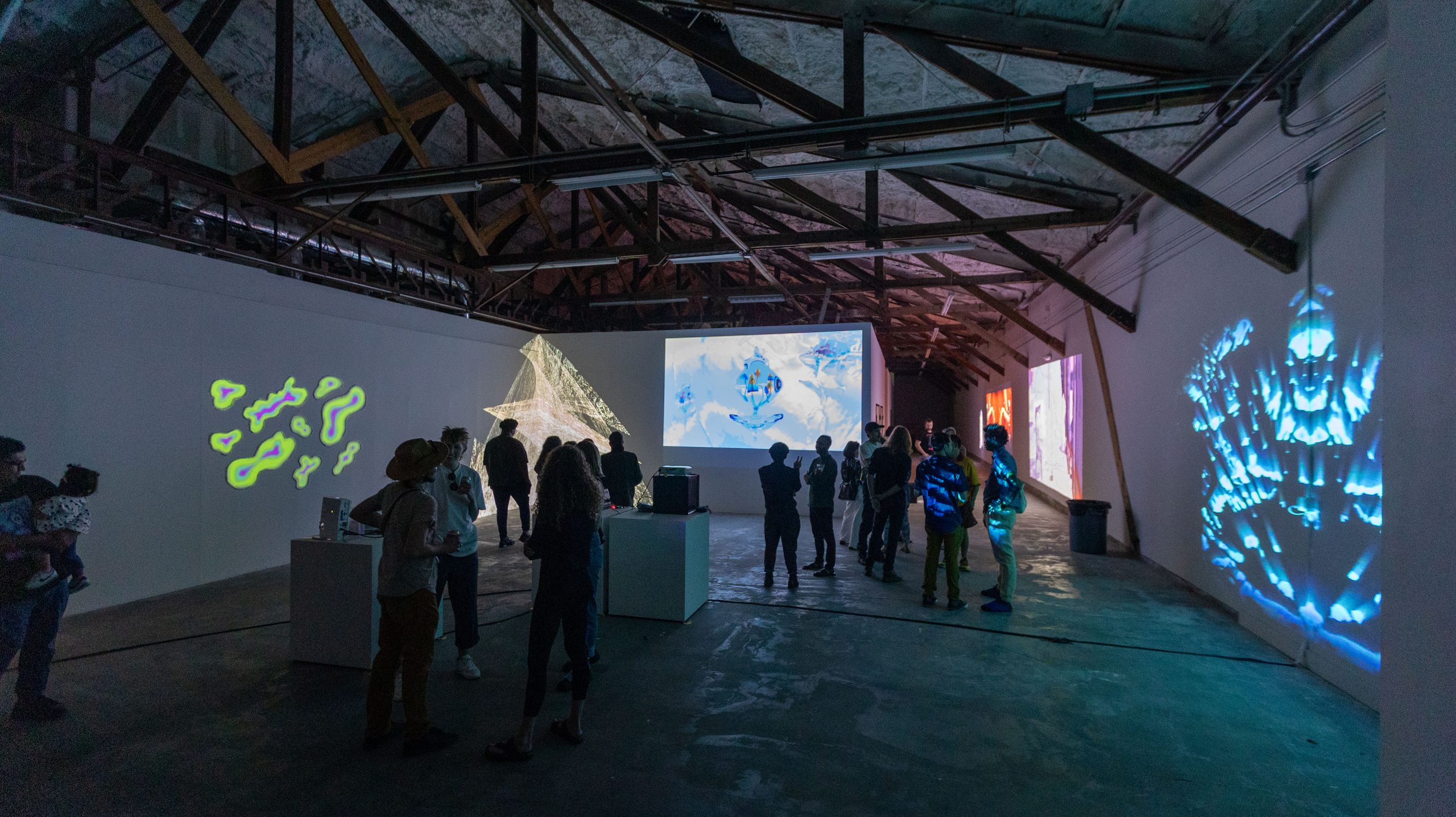 Wide install with yellow projection, paper sculpture, and many-armed figure