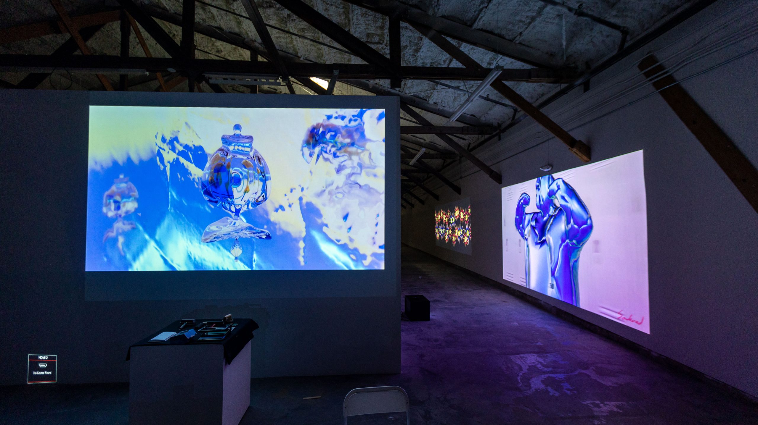 Chrome figure projected on gallery wall alongside abstract liquid imagery
